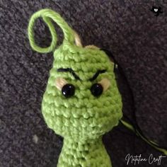 a green crocheted toy with eyes and hair on it's head sitting on the floor