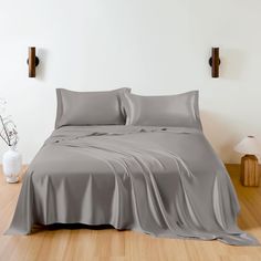 an image of a bed with grey sheets and pillowcases on the wooden floor