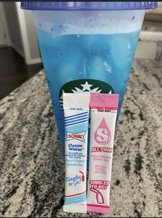 two tubes of toothpaste sitting on top of a counter next to a cup