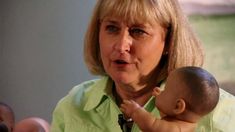 a woman holding a baby doll in her lap and looking at the camera with an angry look on her face