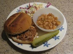 a plate with a sandwich, beans and pickle on it