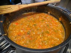 a pot filled with soup sitting on top of a stove next to a wooden spoon