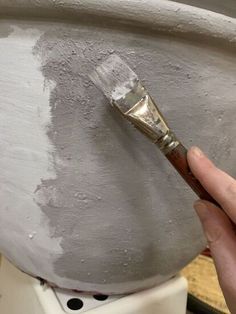 a person holding a paintbrush in front of a large pot with white paint on it