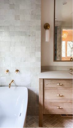 a white bath tub sitting next to a wooden cabinet in a bathroom under a mirror