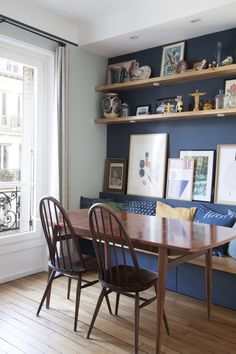 a dining room table and chairs in front of a window with open shelves on the wall