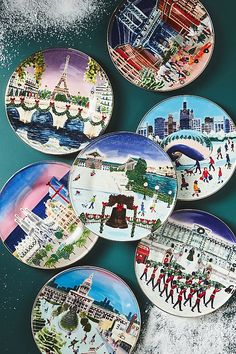 four plates with pictures of people walking in the snow and buildings on them, all painted different colors