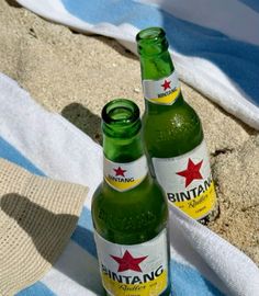 two bottles of beer sitting on top of a towel next to each other in the sand