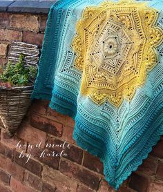 a crocheted blanket hanging on a brick wall next to a potted plant