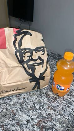 a bag with a face drawn on it sitting next to a bottle of orange juice