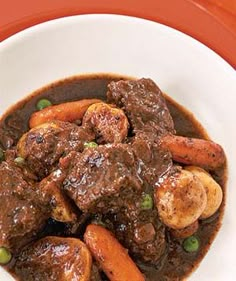 a bowl filled with beef and carrots on top of a white table next to green peas