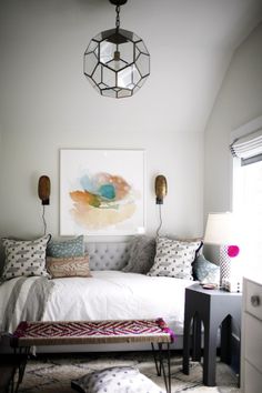 a bedroom with a bed, ottoman and painting on the wall