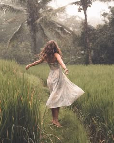 a woman in a dress walking through tall grass