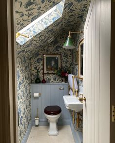 an attic bathroom with blue and white wallpaper on the walls, toilet and sink