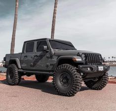 a black jeep parked on the side of a road near some water and palm trees