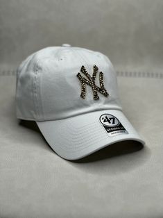 This is a white New York Clean Up adjustable hat that is hand embellished with gold Swarovski crystals on the front logo. This hat features over 150+ smaller Swarovski style crystals. - 100% Cotton - Matching fabric strap & buckle - One Size Fits All - Raised Embroidered Logo - 150+ Swarovski style gold crystals individually placed by hand - Ready to ship in 1 week from San Diego, CA Hat New York, Diy Hats, Yankees Baseball Cap, Bling Hat, Hat Aesthetic, Gold Crystals, New York Yankees Baseball, Chula Vista, Diy Hat