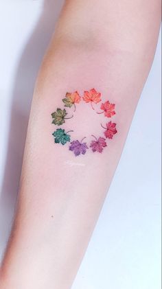 a woman's arm with colorful leaves painted on the side of her arm and in the shape of a circle