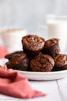 chocolate muffins on a white plate next to a glass of milk and red napkin