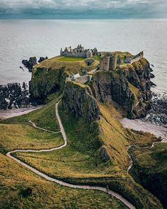 an old castle sits on top of a hill near the ocean and is surrounded by green grass