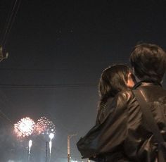 two people looking at fireworks in the night sky with power lines and telephone poles behind them