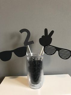 two straws sticking out of the side of a glass with sunglasses on it and one is upside down