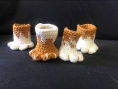 three small crocheted boots with white and orange designs on the bottom, one in the shape of a dog's paw