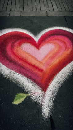 a chalk drawing of a red heart with a green leaf on the sidewalk next to it