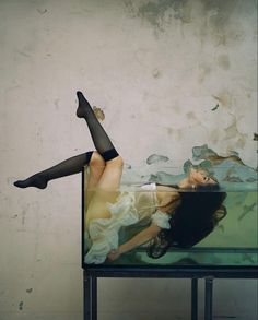 a woman laying on top of a glass table next to a wall with peeling paint