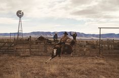 two men are riding horses in an open field with mountains in the background and a windmill