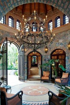 a large foyer with chandelier, chairs and table in front of an arched doorway