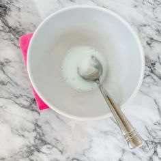 a white bowl with a spoon in it on top of a marble counter next to a pink towel