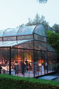 a group of people standing in front of a glass house with lights on the roof