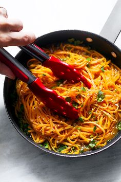 someone using tongs to stir spaghetti in a skillet