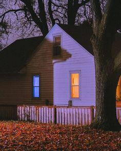 a white house sitting next to a tree with leaves on the ground in front of it