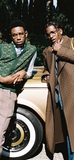 two men standing next to each other in front of a car