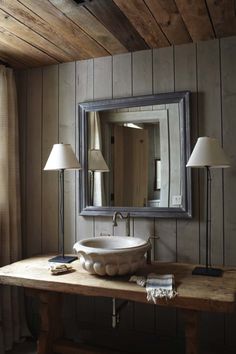 a bathroom sink sitting under a large mirror next to a lamp on top of a wooden table