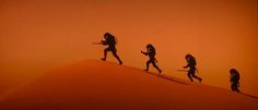 the silhouettes of four people walking up a hill with swords in their hands, against an orange sky