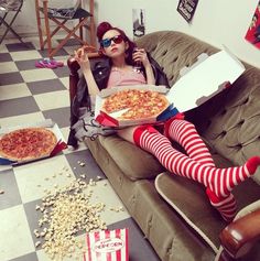 a woman sitting on a couch with pizza and popcorn