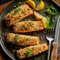 some fish is on a plate with lemons and parsley next to a fork