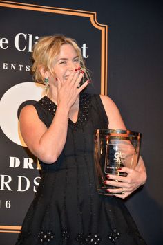 a woman holding an award in front of her face and covering her mouth with both hands