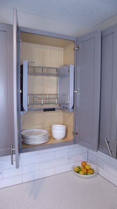 an open cabinet in the middle of a kitchen with plates and bowls on the counter