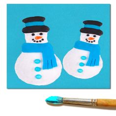 two snowmen with hats and scarfs made out of fondant on a blue background next to an artist's paintbrush