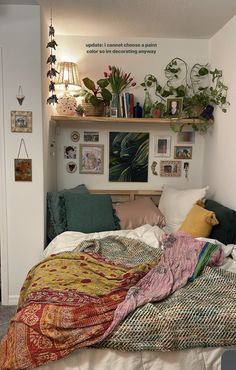 a bed with lots of pillows and blankets on it's headboard next to a shelf filled with plants