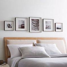 a bed with white linens and pictures on the wall above it in a bedroom