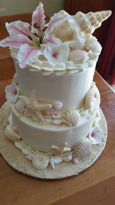 a three tiered cake with seashells and flowers on it