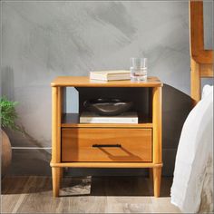 a bedside table with two drawers and a glass on top, next to a bed