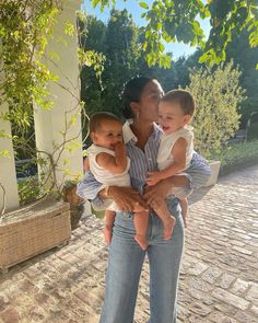 a woman holding two small children in her arms while standing next to a brick walkway