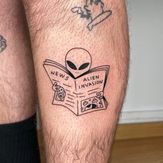 an alien reading a news paper tattoo on the leg, next to another man's legs