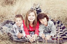 three people sitting on a blanket in the middle of some tall grass with a cat behind them