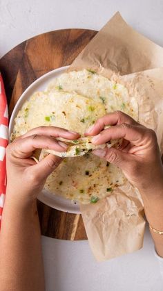 two hands grabbing food from a plate on top of a wooden table with napkins