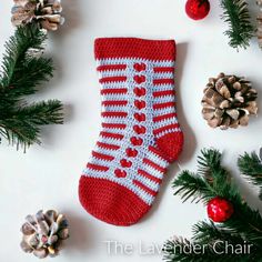 a crocheted christmas stocking with pine cones and ornaments around it on a white surface